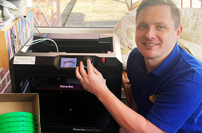 Andy Lee, Curriculum Leader for Engineering at SCG crouching next to 3D printer